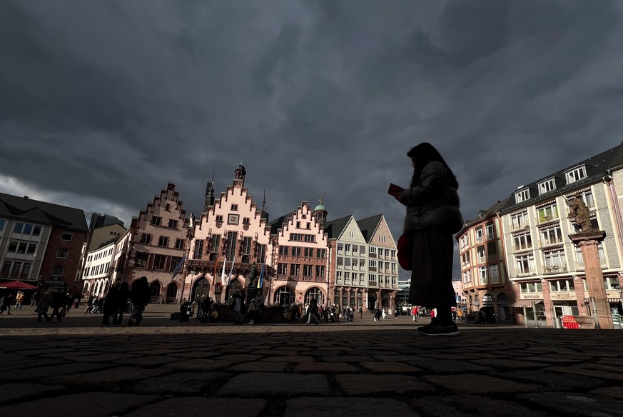 ARCHIV - 31.01.2024, Hessen, Frankfurt/Main: Unter einem dunklen Wolkenhimmel leuchtet das Rathaus R�mer in Frankfurt im Sonnenschein. (zu dpa: �Tr�bes Wetter am Wochenende in Hessen - Gewitter am Sam ...