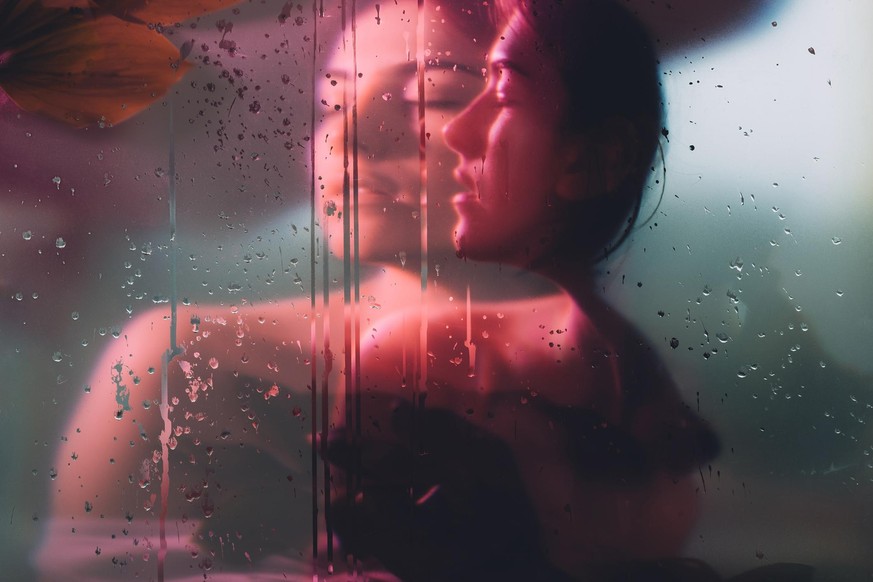 Nature portrait. Pure soul. Sensual woman face blur silhouette in neon red bokeh light behind steamed glass with rain drops double exposure effect. Beauty wellness. Dreamlike freshness.