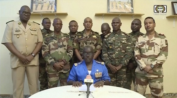 HANDOUT - 26.07.2023, Niger, Niamey: In diesem Bild aus einem von ORTN zur Verfügung gestellten Video gibt Oberstmajor Amadou Abdramane (vorne, M) am späten Mittwoch eine Erklärung ab, während eine De ...