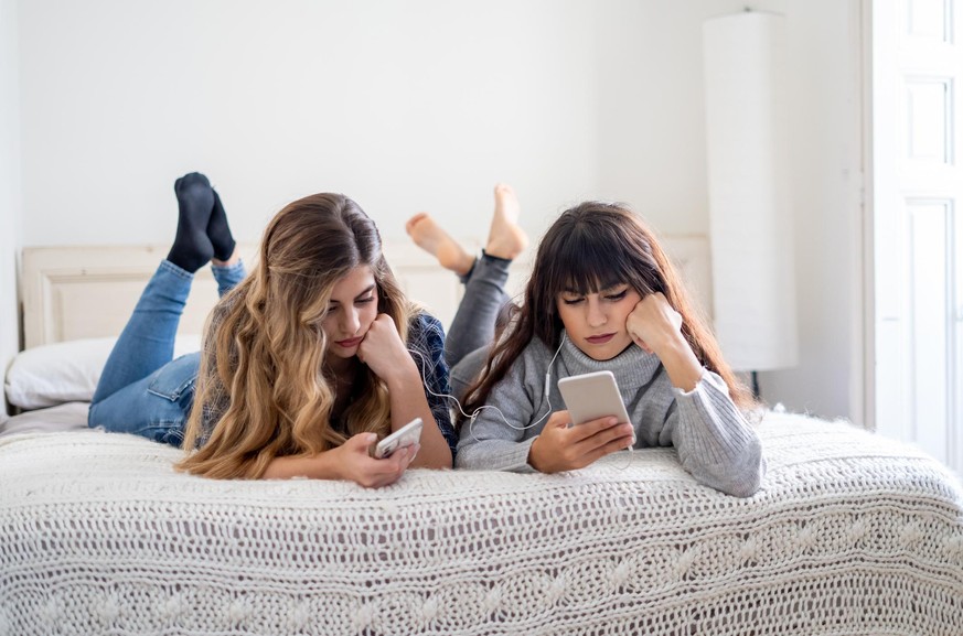 COVID 19 Outbreak. Bored depressed girlfriends flatmates online using mobile phones at home in isolation during quarantine. Impact on mental health during coronavirus lockdown and social distancing.