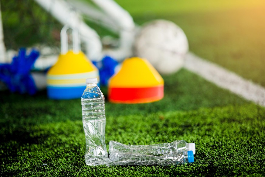 Plastic bottles with blurry soccer training equipment on artificial turf. It is waste from soccer training or football match.