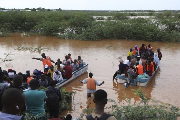28.04.2024, Kenia, Garissa: Menschen durchqueren ein überflutetes Gebiet, in dem ein anderes Boot mit einer Gruppe von Menschen an Bord in Mororo an der Grenze zwischen den Bezirken Tana River und Gar ...