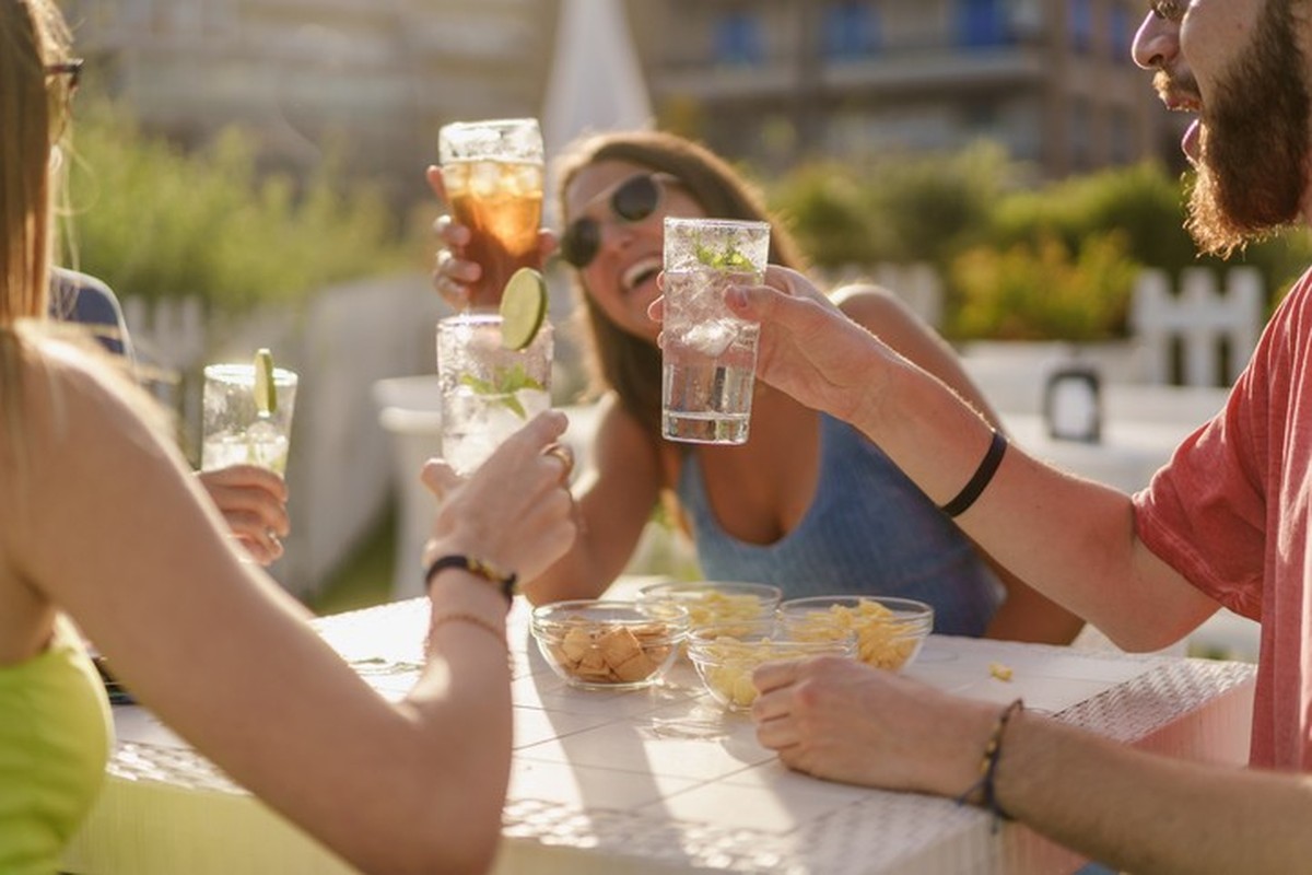 Happy hour toasting. Young friends clinking with fresh mojitos sitting in a counter restaurant and taking aperitif in the summer. Friendship and togetherness concept
