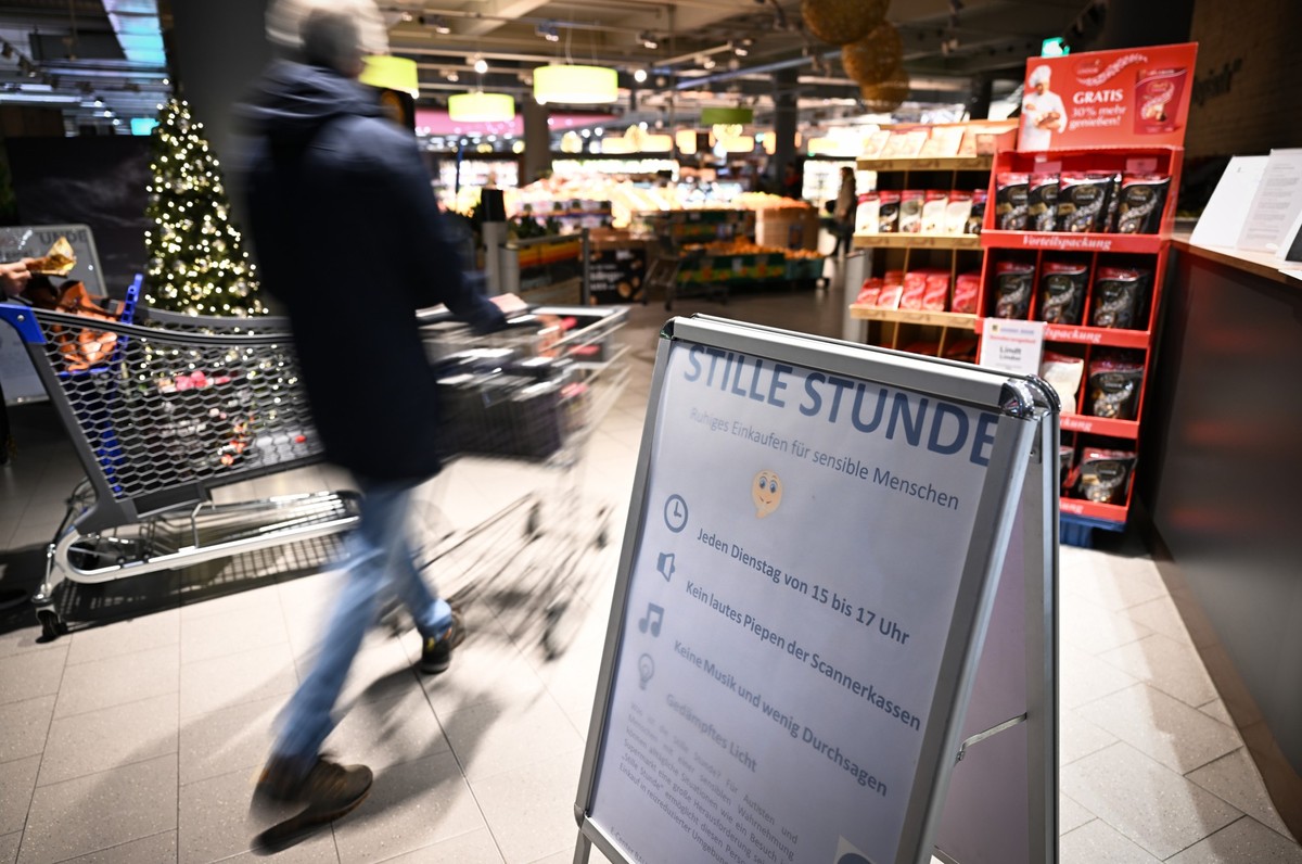 PRODUKTION - 12.12.2023, Baden-Württemberg, Konstanz Am Bodensee: Ein Mann schiebt seinen Einkaufswagen in den Supermarkt, während im Vordergrund ein Schild auf die Stille Stunde im Edeka hinweist. (z ...