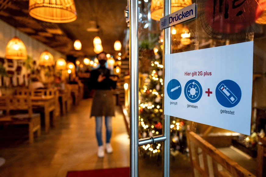 Ein Schild an der Tür eines Restaurants weist auf die 2G-Plus-Regel hin. Vollständig gegen das Coronavirus geimpft oder von einer Covid-Infektion genesen, ist vielerorts für zahlreiche Aktivitäten in  ...