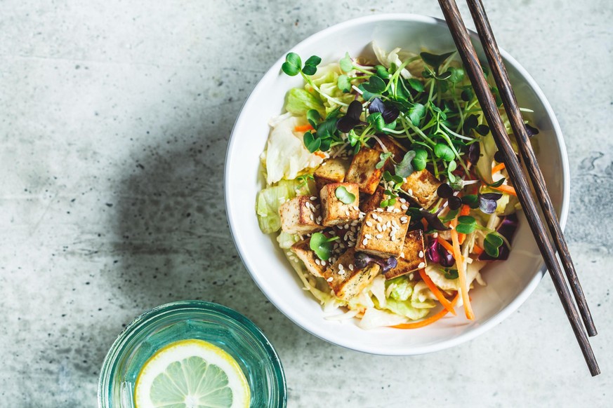 Fried tofu salad with sprouts and sesame seeds in a white bowl. Vegan food, asian food concept.