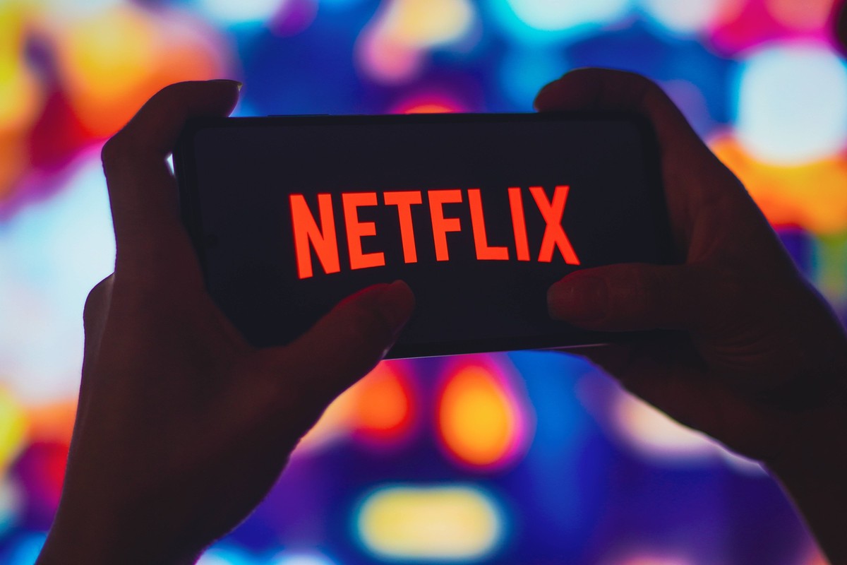 July 6, 2022, Brazil. In this photo illustration, a silhouetted woman holds a smartphone with the Netflix logo displayed on the screen. July 6, 2022, Brazil. In this photo illustration, a silhouetted ...