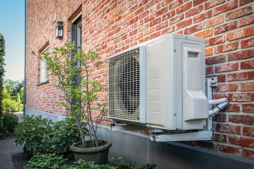 Side view of outdoor energy unit hanging on brick wall of beautiful house on a sunny day. Air conditioner or air heat pump. Outdoor unit powered by renewable energy.