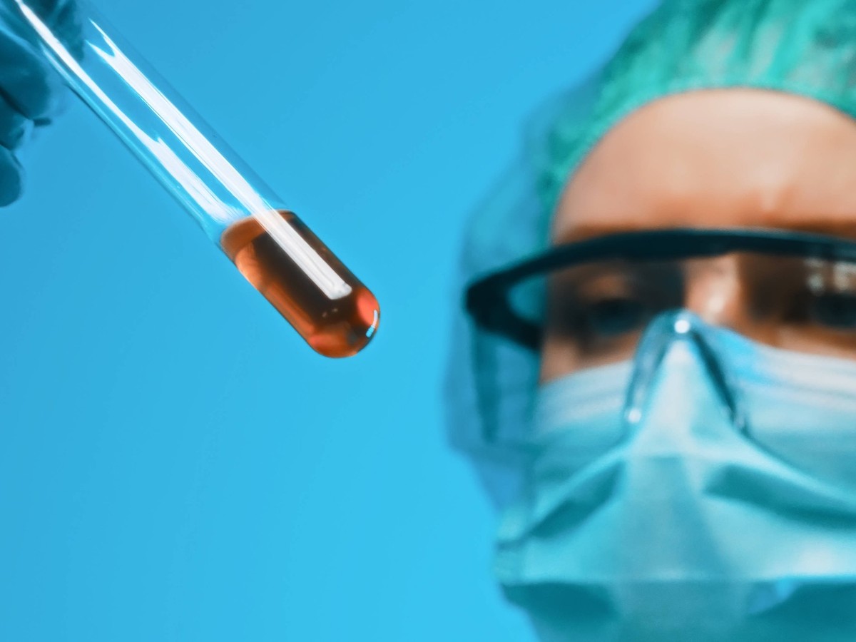 Frau mit Schutzbrille und Maske bei der Arbeit mit Reagenzgl