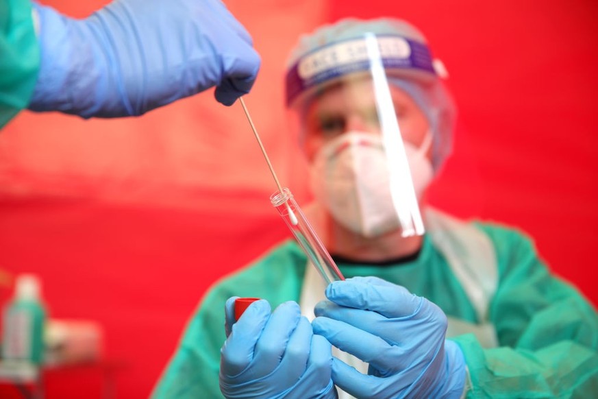 BONN, GERMANY - AUGUST 24: An employee of the Bonn professional firefighters places a throat swab sample into a tube held by a colleague from a woman seeking a test for possible Covid-19 infection dur ...