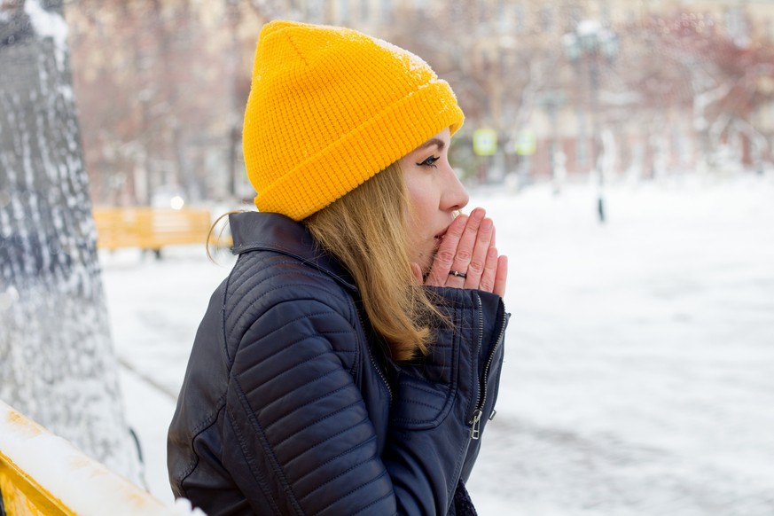 beautiful young woman warming her hands on the street in winter