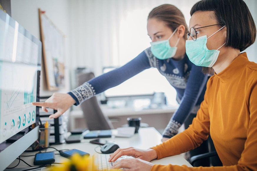 Two female colleagues at work wearing face protective mask, to protecting themselves against corona virus