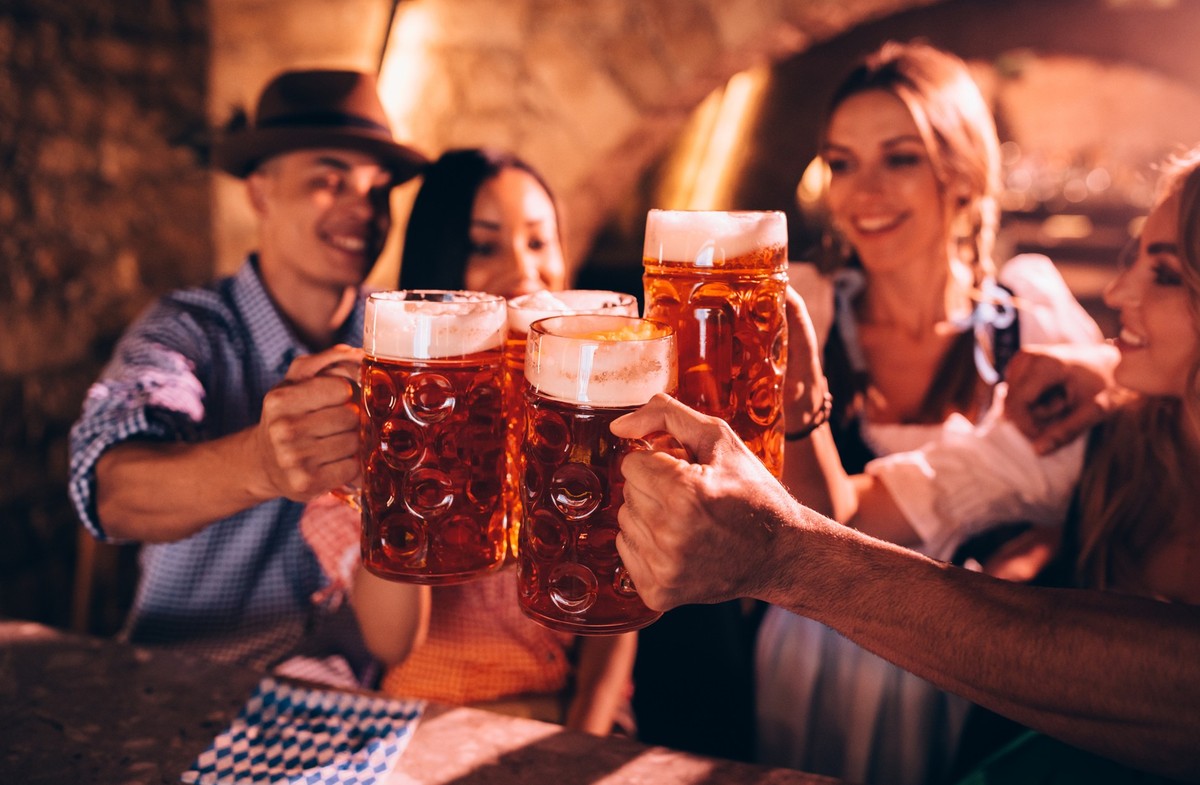 Happy multi-ethnic friends in traditional Bavarian costumes celebrating Beer Fest and toasting with beer steins