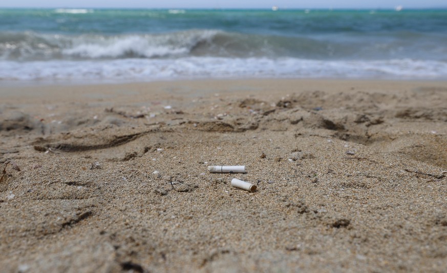 Zigarettenstummel liegen im Sand am Strand der Bucht Cala Estancia. Seit 17.07.2019 gilt hier ein Rauchverbot. Bislang handele es sich jedoch lediglich um eine Empfehlung: Badegäste, die das Verbot mi ...