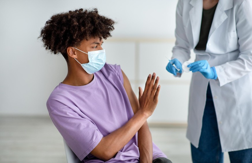 Black teenager stopping medical worker from making covid vaccine shot, being afraid of coronavirus immunization at clinic. African American adolescent scared of corona vaccination