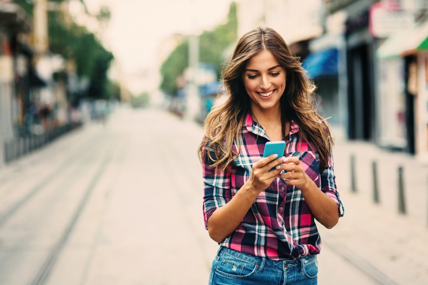 A young woman texting on the phone outdoors.