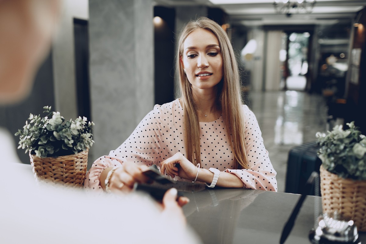 Young beautiful woman hotel guest paying for her stay with credit card at front desk close up