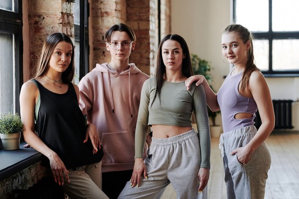 Three teenage girls and guy in activewear standing by window in modern loft studio and looking at camera after vogue dance training