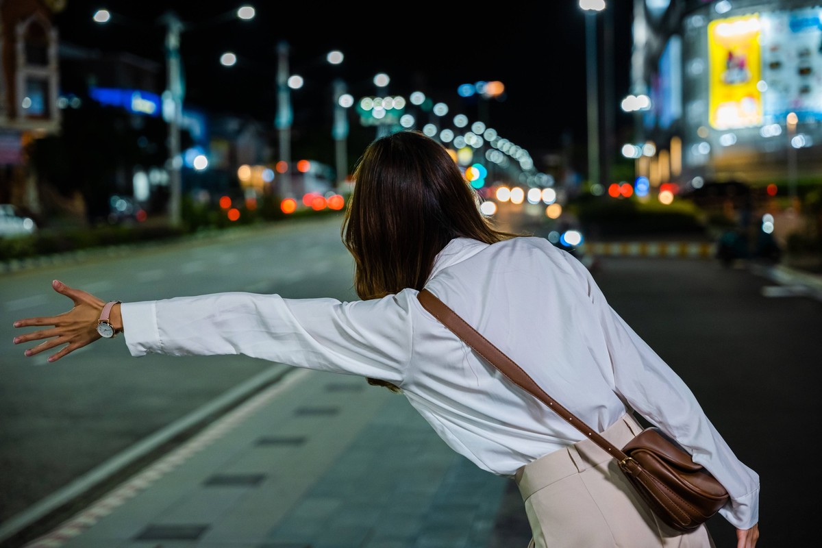businesswoman standing hail waving hand taxi on road in busy city street at night Asian business woman hail waving hand taxi on road in city street at night, Beautiful woman smiling using smartphone a ...