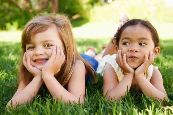 Shot of two adorable little girls lying next to each other on the grass