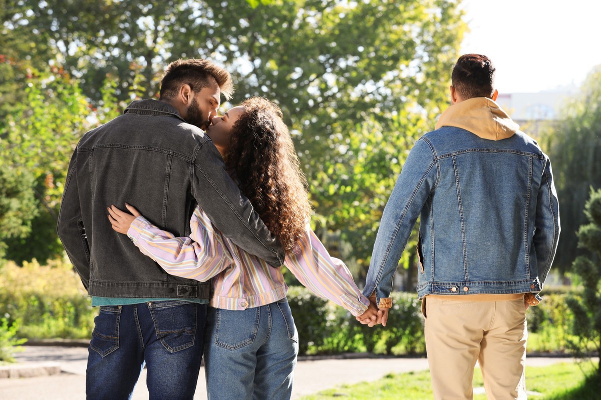 Woman kissing another man while holding hands with her boyfriend during walk in park, back view. Love triangle Model Released Property Released xkwx background, people, jealousy, park, love, concept,  ...