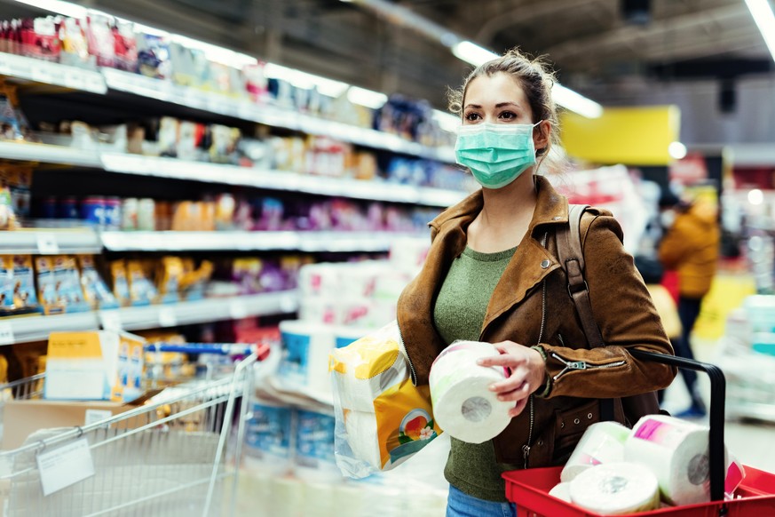 Young woman with protective mask shopping toilet paper and making supplies during virus pandemic.