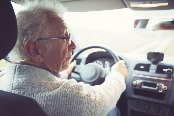 Friendly old gentleman with metal frame glasses drives car