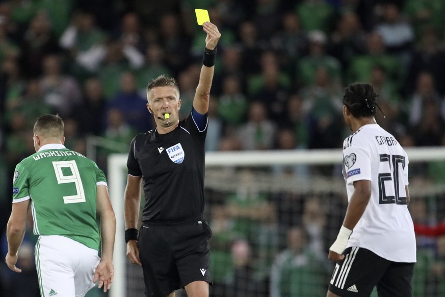 Referee Daniele Orsato shows a yellow card to Germany's Serge Gnabry, right, during the Euro 2020 group C qualifying soccer match between Northern Ireland and Germany at Windsor Park, Belfast, Norther ...