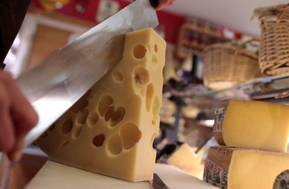 A picture taken on May 29, 2015 in Paris shows a cheese vendor cutting a piece of Emmental cheese. A Swiss agricultural institute discovered that tiny specks of hay are responsible for the famous hole ...