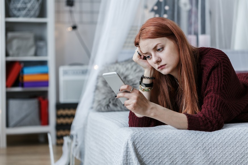 Worried, young teenager looking at the phone in her room