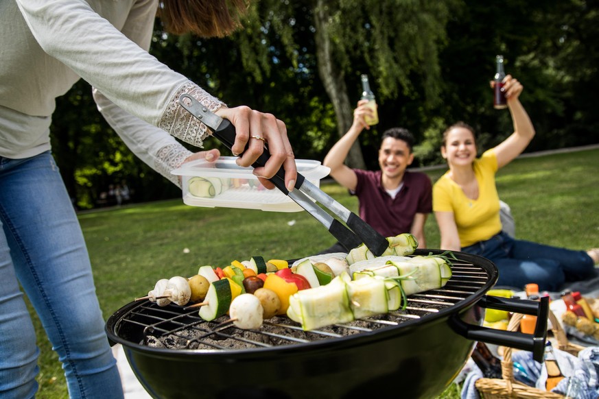 ILLUSTRATION - Eine Frau legt am 23.07.2020 in Hamburg in einem Park Gemuesespiesse auf einen heissen Grill, waehrend im Hintergrund zwei Freunde sitzen (gestellte Szene). Foto: Christin Klose || Mode ...