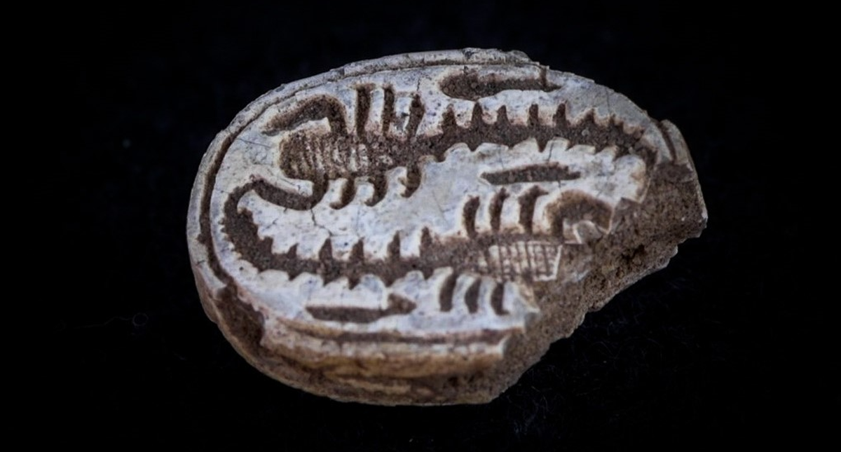 Das Amulett hat die Form eines Mistkäfers, darauf sind zwei Skorpione abgebildet.