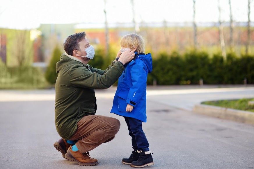 Mature man wearing a protective mask puts a face mask on a his son in airport, supermarket or other public place. Safety during COVID-19 outbreak. Epidemic of virus covid. Coronavirus pandemic.