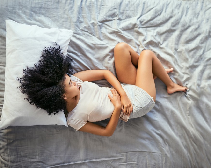 Shot of a young woman suffering from stomach cramps in her bedroom