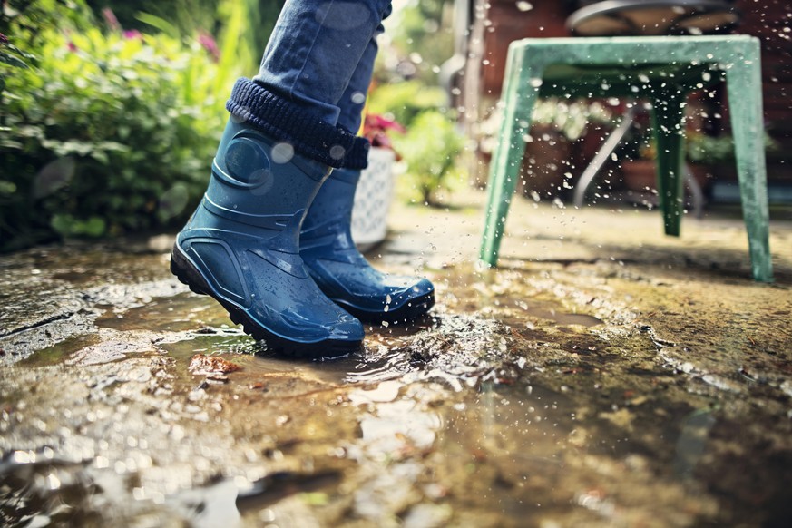 Closeup of galoshes in puddle. Little boy is splashing after rain.