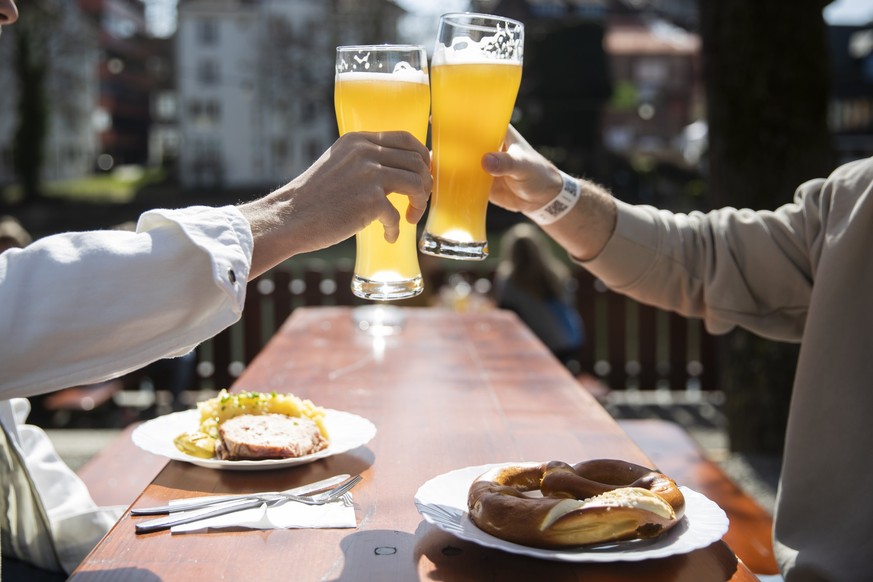 ARCHIV - 28.03.2021, Baden-Württemberg, Tübingen: Zwei Menschen sitzen bei gutem Wetter in einem Biergarten und stoßen mit einem Bier an.Der Regenschirm kann dieses Wochenende im Schrank bleiben, doch ...