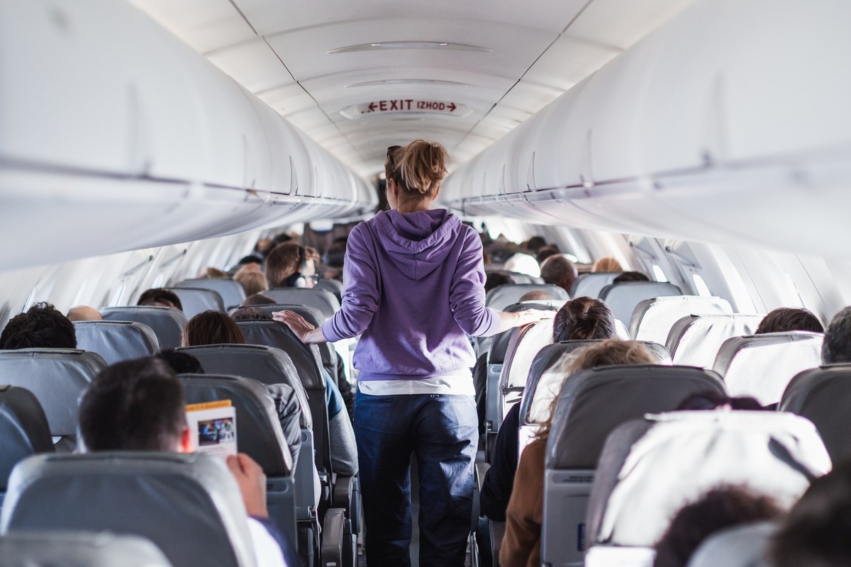 Interior of airplane with passengers on seats and female traveler walking the aisle. Commercial economy flight service concept., Interior of airplane with passengers on seats and female traveler walki ...