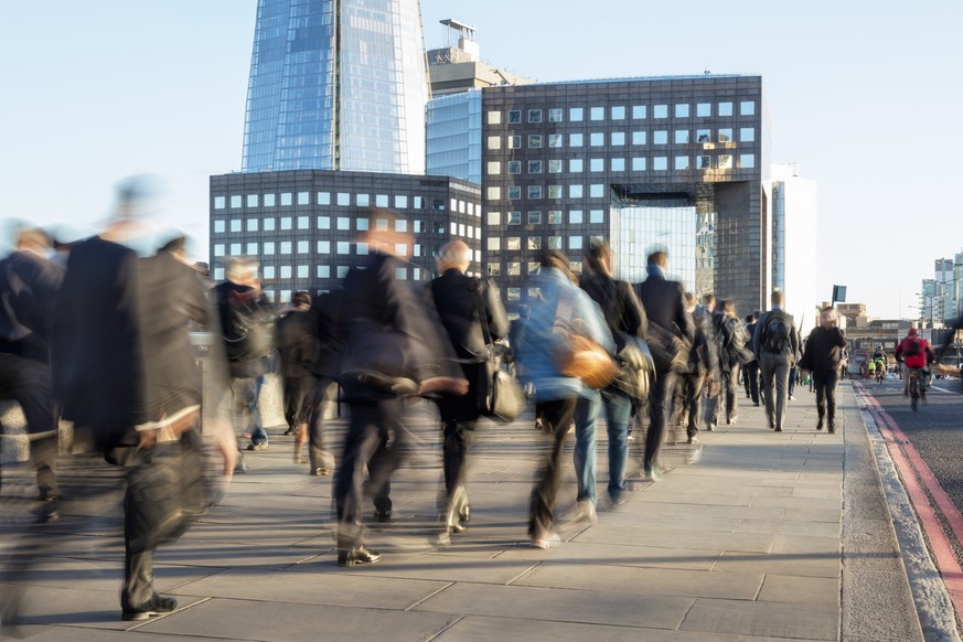 Blurred image of business commuters crossing London Bridge, office buildings with The Shard are visible in the background, London, England