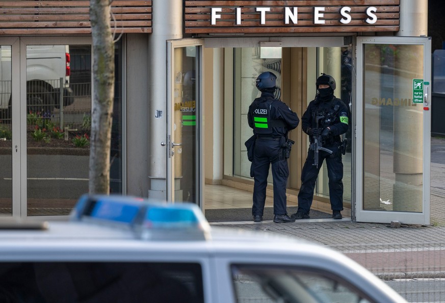 18.04.2023, Nordrhein-Westfalen, Duisburg: Polizisten stehen nach einer Attacke in einem Fitnessstudio in der Innenstadt im Eingangsbereich des Studios. Nach der blutigen Attacke in einem Duisburger F ...