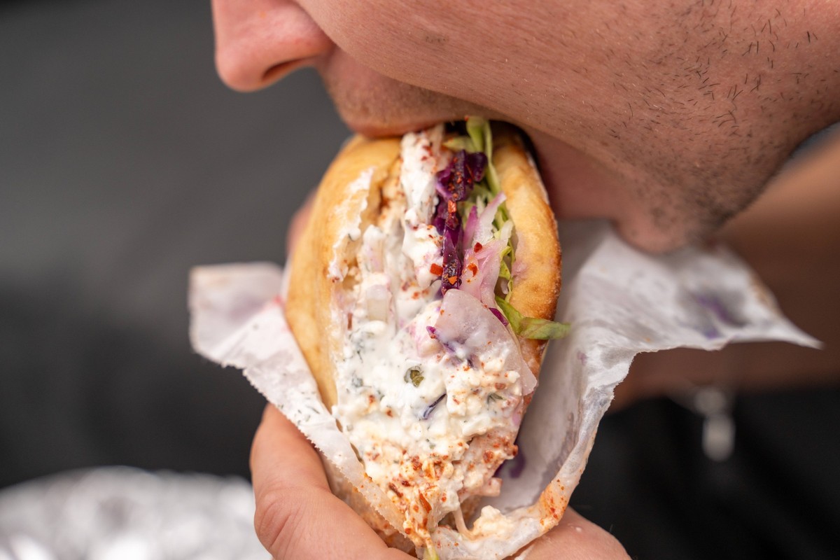 Augsburg, Bavaria, Germany - October 17, 2023: A man bites into a vegetarian kebab kebap without meat with lots of yogurt sauce *** Ein Mann bei