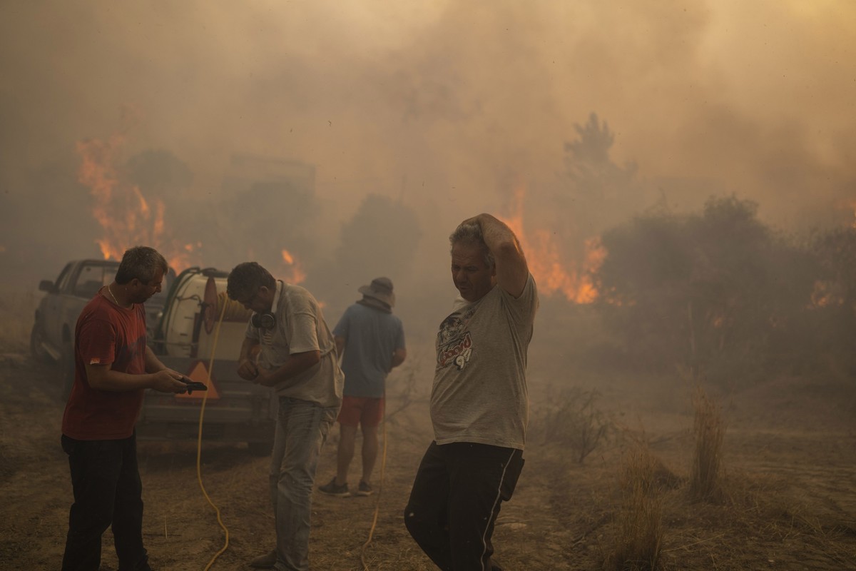25.07.2023, Griechenland, Gennadi: Einheimische versuchen einen Waldbrand im Dorf Gennadi zu löschen. Freiwillige Helfer und Dorfbewohner haben am Dienstagabend das Dorf Gennadi im Südosten der Insel  ...
