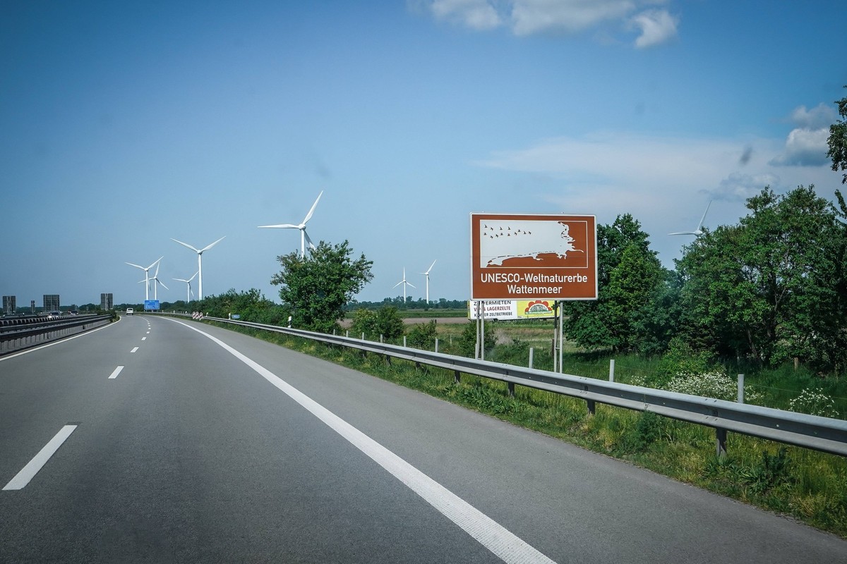 Autobahn, Straßenschild, UNESCO-Weltnaturerbe Wattenmeer, braunes Schild, Windräder, blauer Himmel, Autobahn A31, Verkehrsschild, Auto, Fahrbahn, Leitplanke, Bäume, Deutschland, Verkehr, Sommer, Wegwe ...