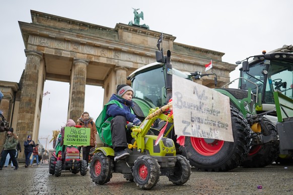 13.01.2024, Berlin: Kinder fahren auf ihren Spielzeug-Traktoren im Rahmen einer kleinen Protest-Aktion der Landwirtschaftsjugend vor dem Brandenburger Tor entlang. Viele Landwirte haben sich bereits a ...