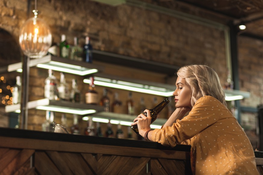 Bad day. Pretty blonde woman sitting at the bar counter and seeping beer while being upset with something