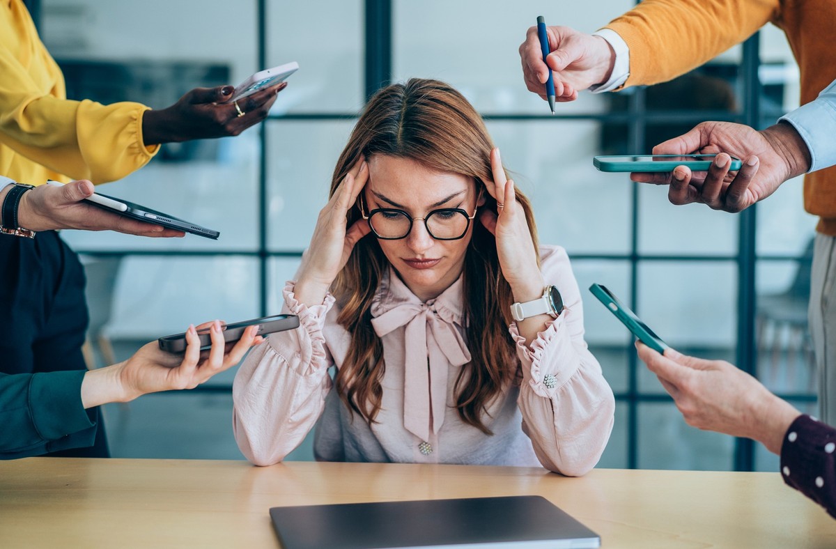 Shot of a stressed out businesswoman surrounded by colleagues needing help. Businesswoman feeling stressed out in a demanding office environment at work. Photo of businesswoman under strain as colleag ...