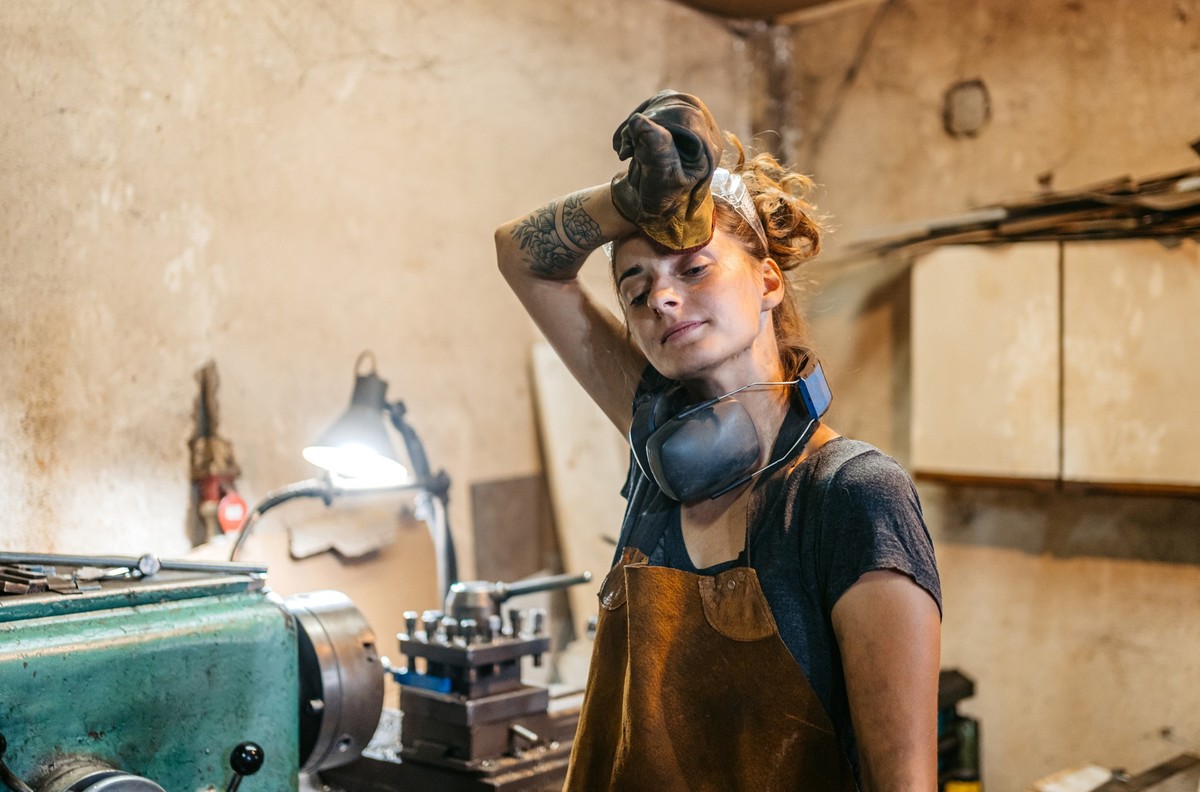 Young female welder wiping the sweat off her forehead in a metal workshop.