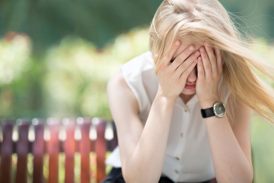 Portrait of young woman covering her face with both hands in defeat and frustration