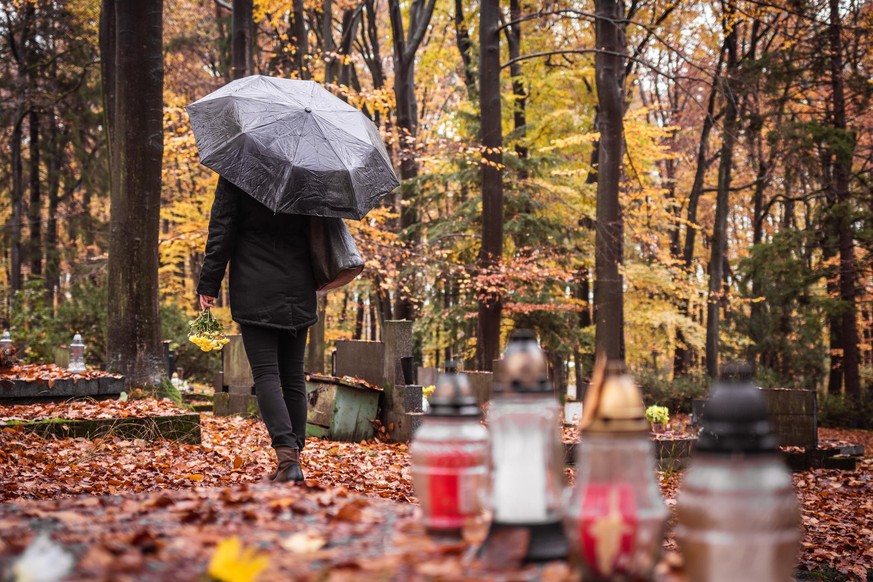 Lonely sad woman with umbrella mourning for dead person at grave in cemetery. Last goodbye for dead person.