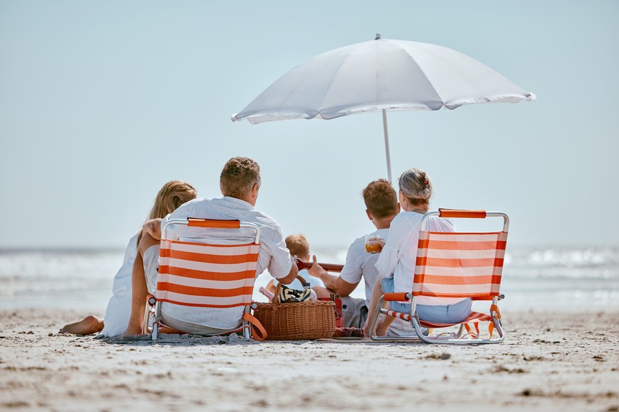 Beach, umbrella and big family on a summer vacation, trip or seaside journey together in Australia. Travel, relax and children on a holiday adventure with their grandparents and parents by the ocean.