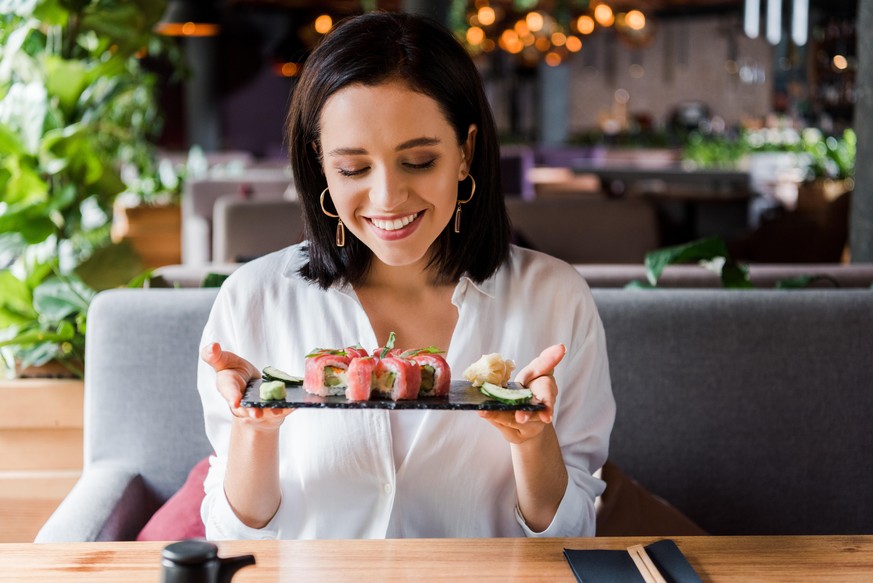 happy woman holding plate with tasty sushi in restaurant